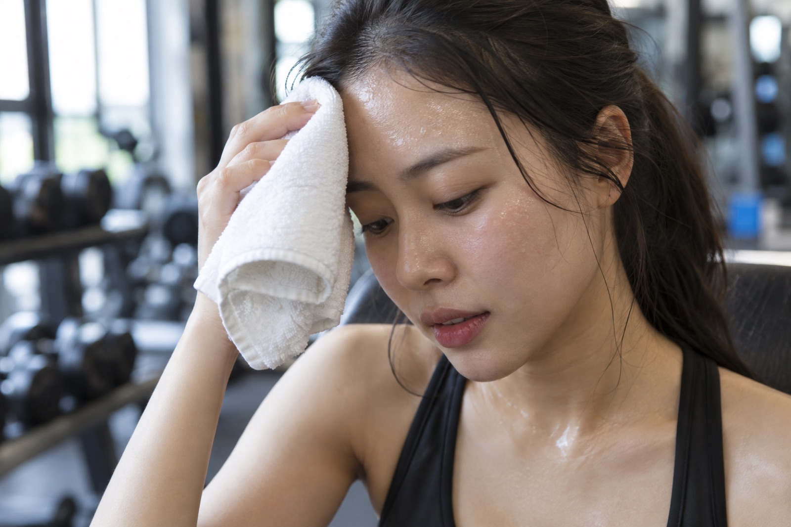 헬스장 벤치에 앉아 깨끗한 수건으로 이마의 땀을 가볍게 두드려 닦는 20대 여성